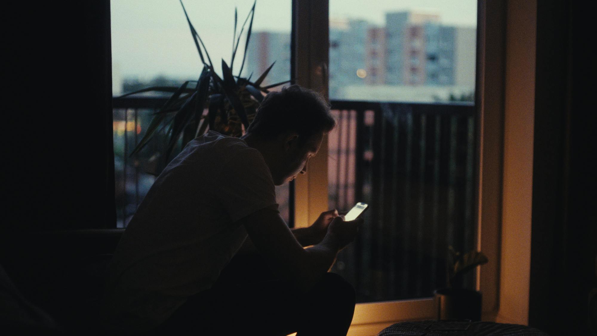 a dark room where a man is on the phone and sitting on a couch